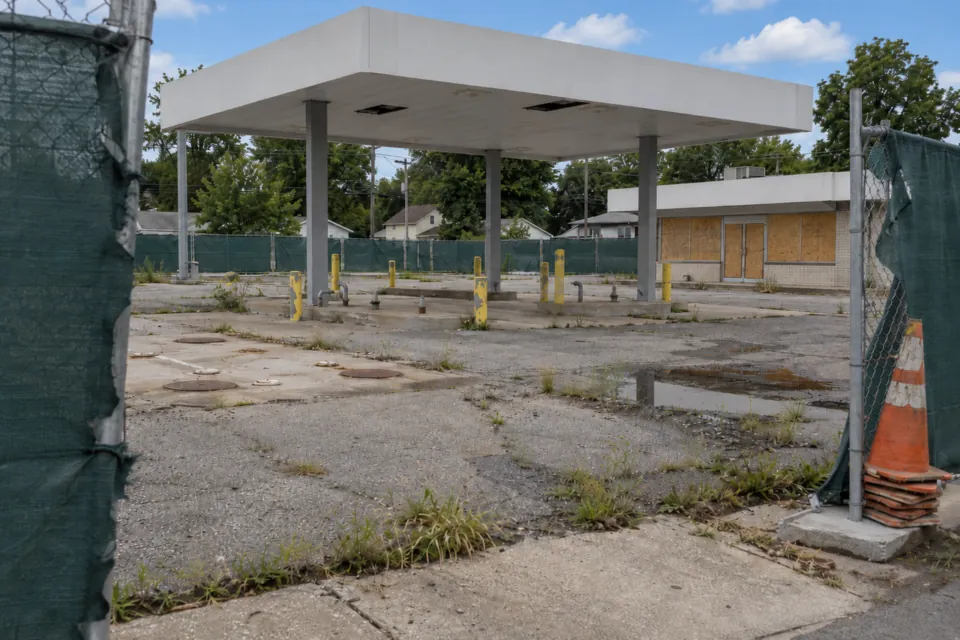 Closed gas station with an empty canopy and pump islands behind a temporary fence with green privacy screening