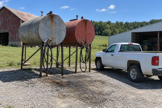 Two aboveground diesel tanks on steel stands in a farmyard on a sunny summer day, with a pickup parked beside them