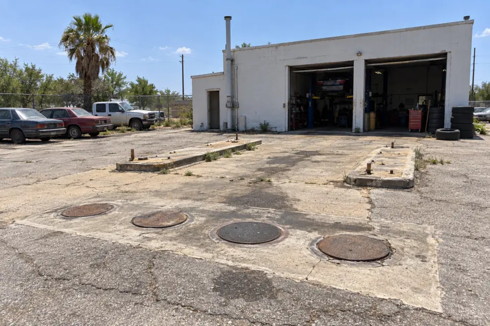 Former gas station now used as a repair shop, with old tank manhole covers still in the pavement