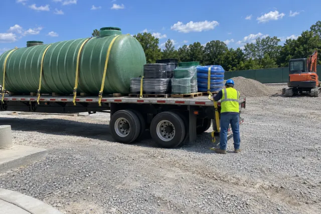 Flatbed trailer delivering a new fiberglass underground tank and pallets of fittings to a gas station construction site