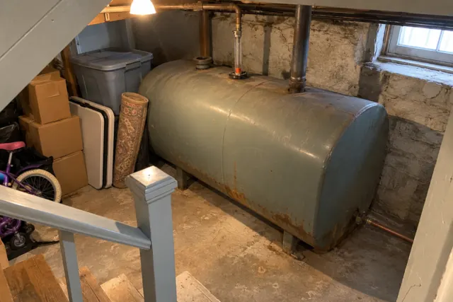 Heating oil tank tucked under the basement stairs, seen from halfway down the steps